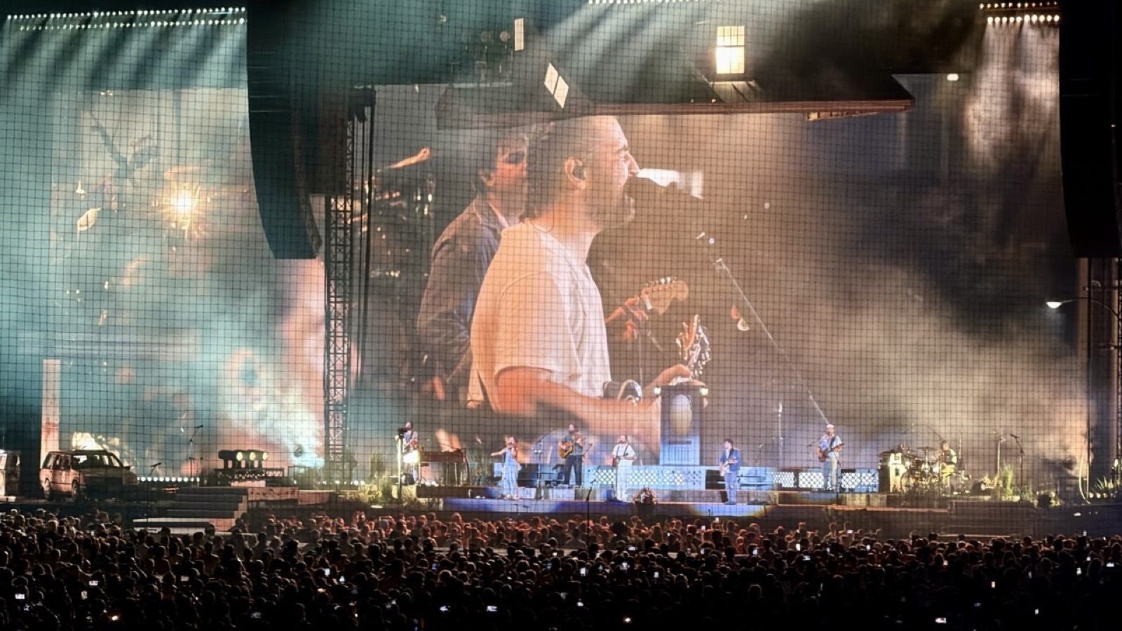 Noah Kahan performing at Wrigley Field, his face filling the giant screen above the stage as the full band plays below
