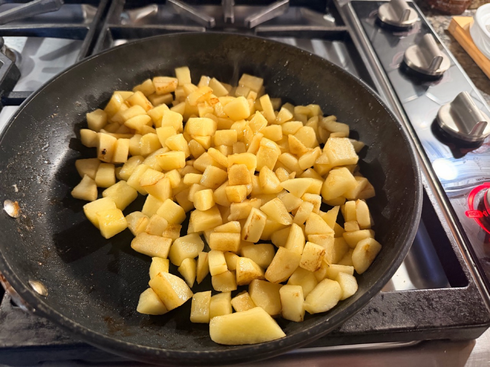 Diced peeled apples sautéing in a skillet, with golden edges beginning to form.